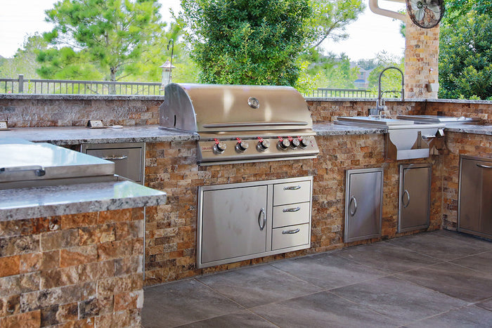 Built-in Blaze stainless steel gas grill with storage drawers, sink, and stone veneer outdoor kitchen design.