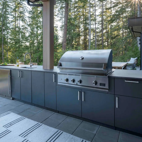 dcs stainless steel gas grill appliance in an urban bonfire outdoor kitchen with a woods background