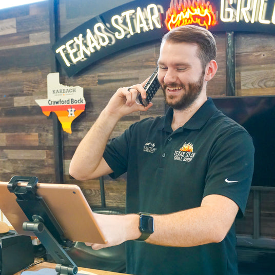 Texas Star Grill Shop team member assisting a customer by phone while using a tablet at the front counter.