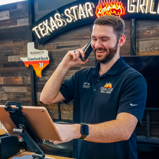 A smiling Texas Star Grill Shop employee taking a phone order while looking at a tablet POS system.