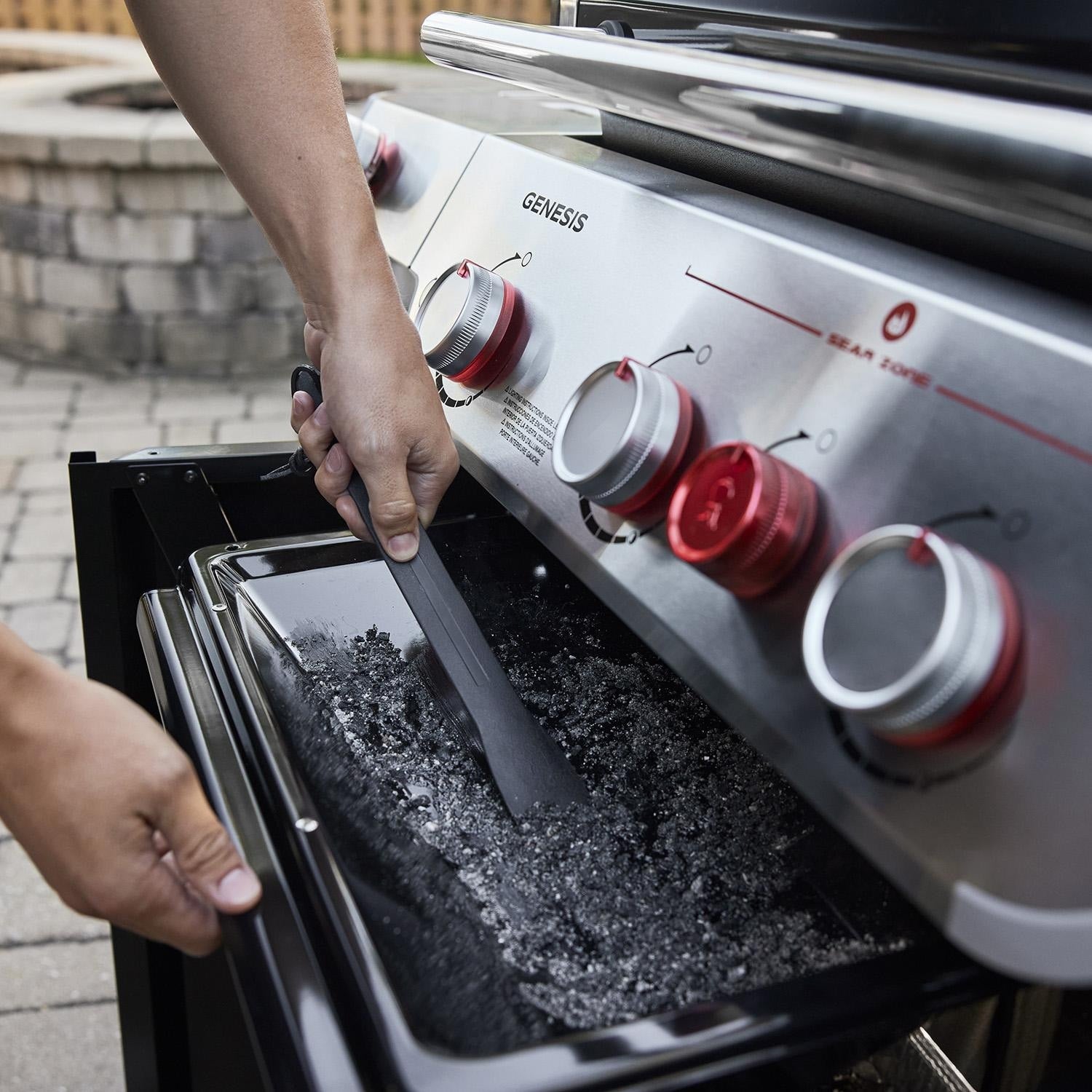 User scraping the grease tray under Weber Genesis SP-S-325 with provided tool