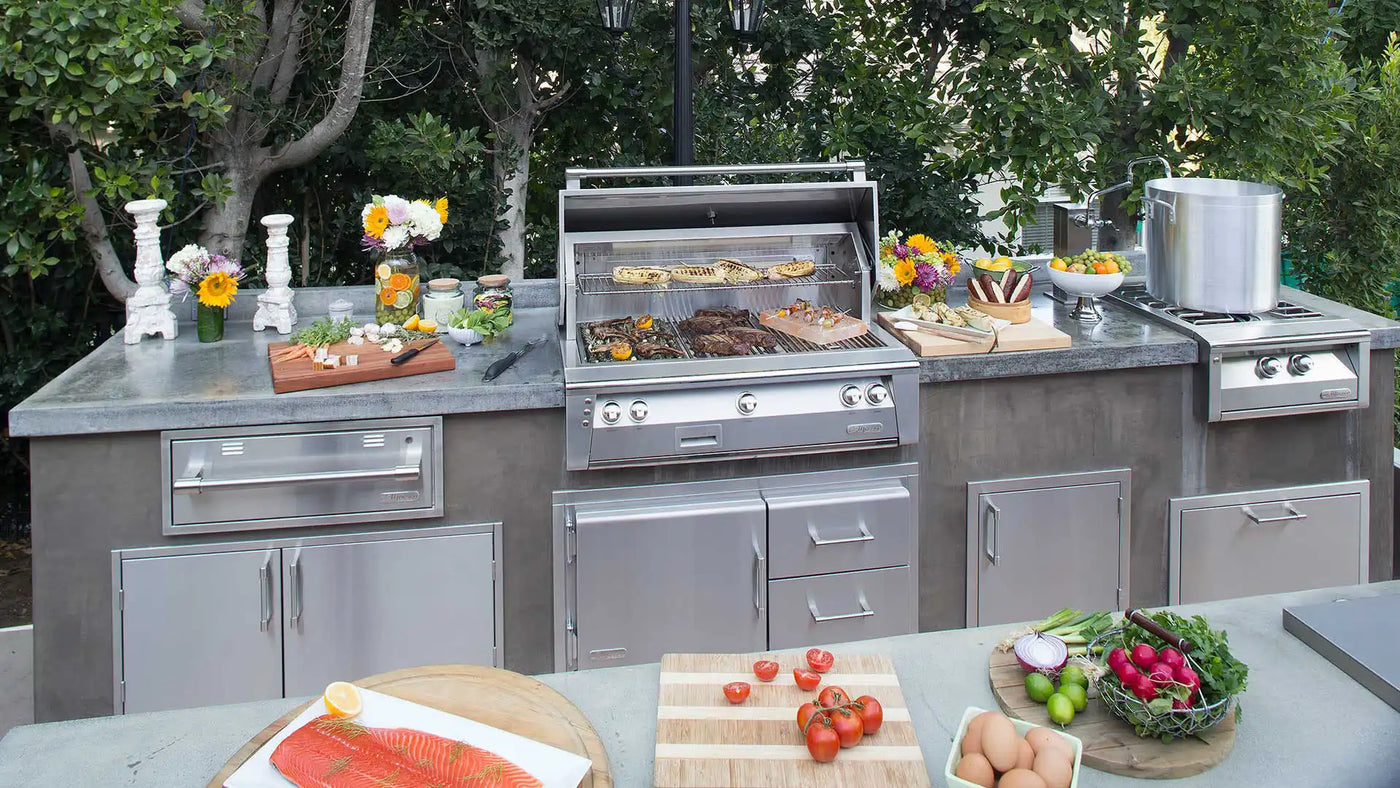 Alfresco built-in stainless steel gas grill and side burner installed in a custom concrete outdoor kitchen island, with fresh salmon and vegetables being prepped on the counter.