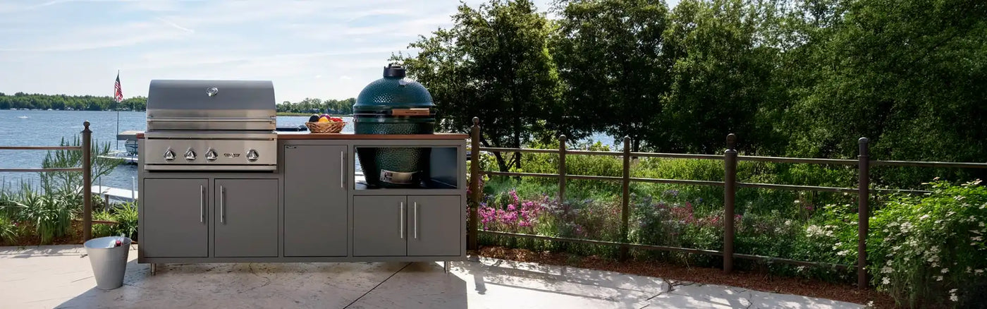 Challenger Designs grey aluminum modular outdoor kitchen island featuring a built-in stainless steel gas grill and a green kamado smoker on a lakeside patio.