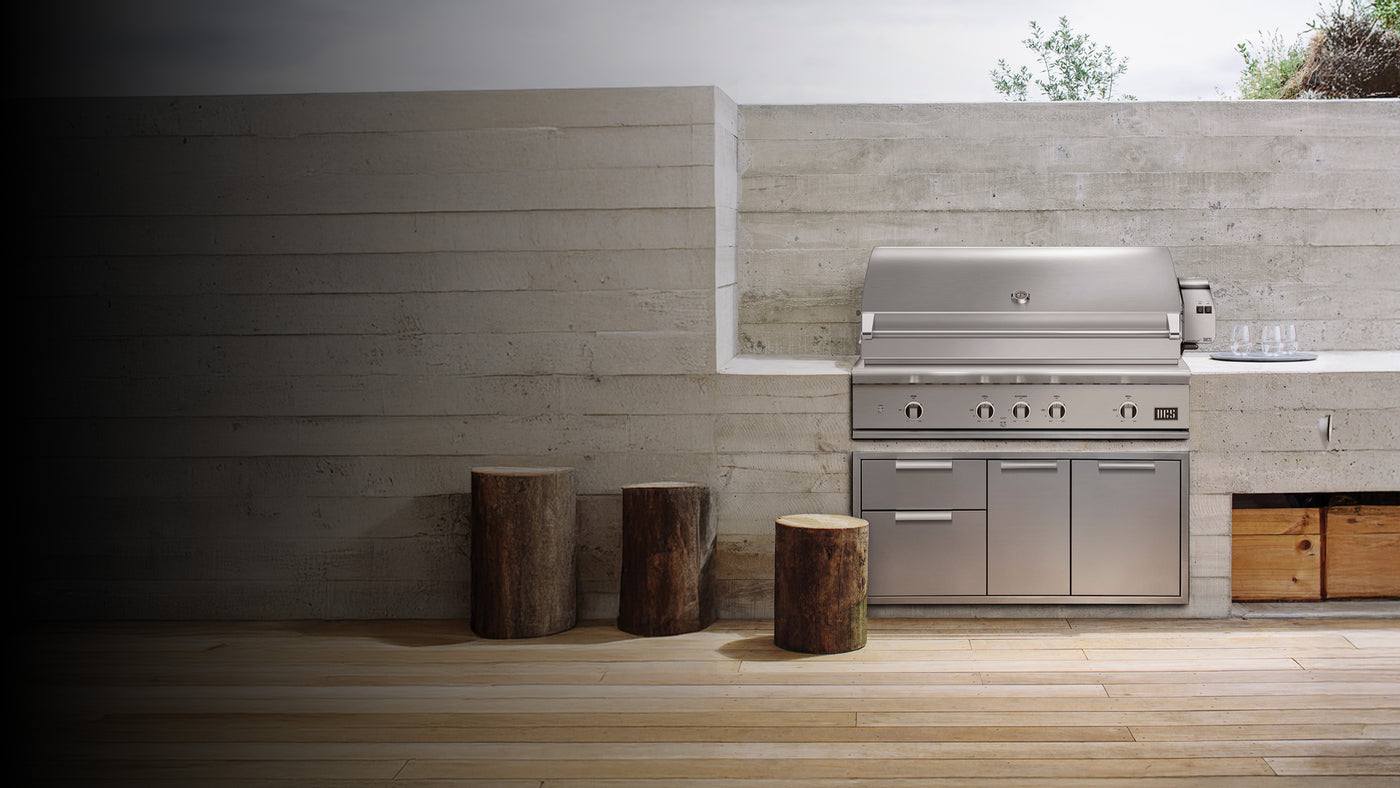 Luxury DCS outdoor kitchen setup with built-in stainless steel grill and cabinetry, set against a modern concrete patio backdrop.