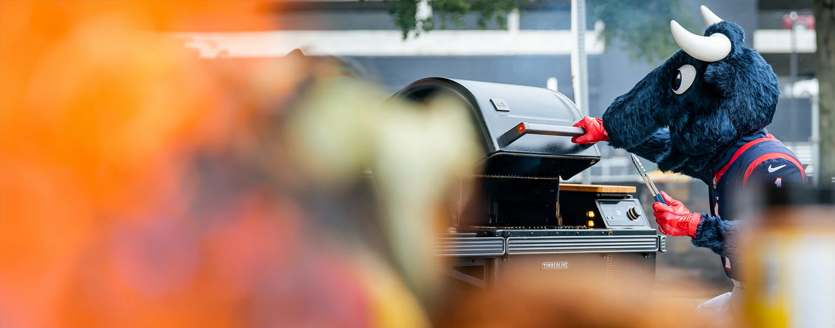Houston Texans mascot grilling on a Traeger Timberline pellet grill at an outdoor tailgate event outside Texas Star Grill Shop.