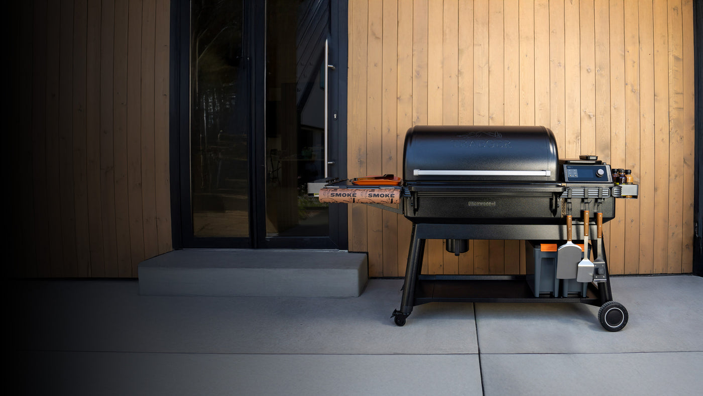 Traeger Ironwood XL pellet grill on a modern patio with wooden paneling, complete with grilling tools and accessories.