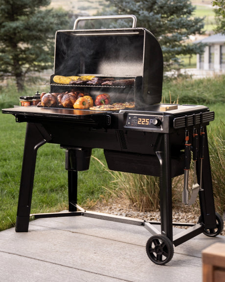 Traeger Woodridge pellet grill loaded with ribs, chicken, vegetables, and pizza on a backyard patio, set to 225°F.