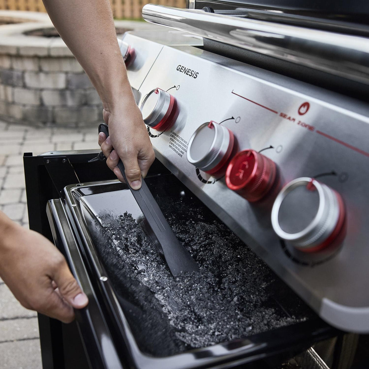 User scraping the grease tray under Weber Genesis SP-S-325 with provided tool