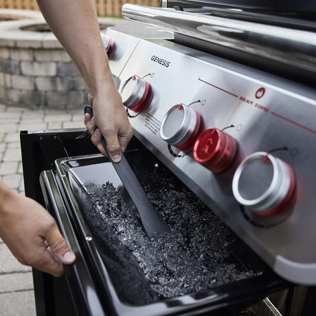 User scraping the grease tray under Weber Genesis SP-S-325 with provided tool